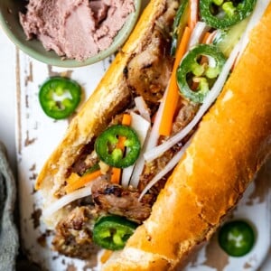 Lemongrass pork banh mi on a white board next to a bowl of pate