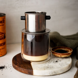 Vietnamese coffee in a coffee cup with a Vietnamese filter on top.