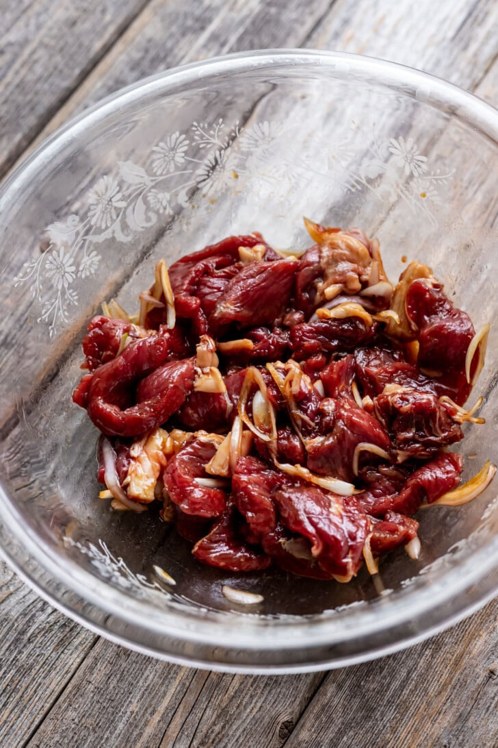 Ribeye steak marinating in a mixing bowl.