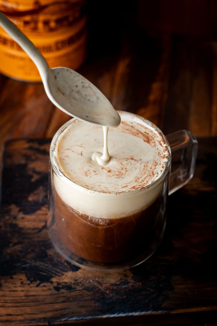Vietnamese egg coffee in a coffee mug. A spoon is scooping some condensed milk from the top.