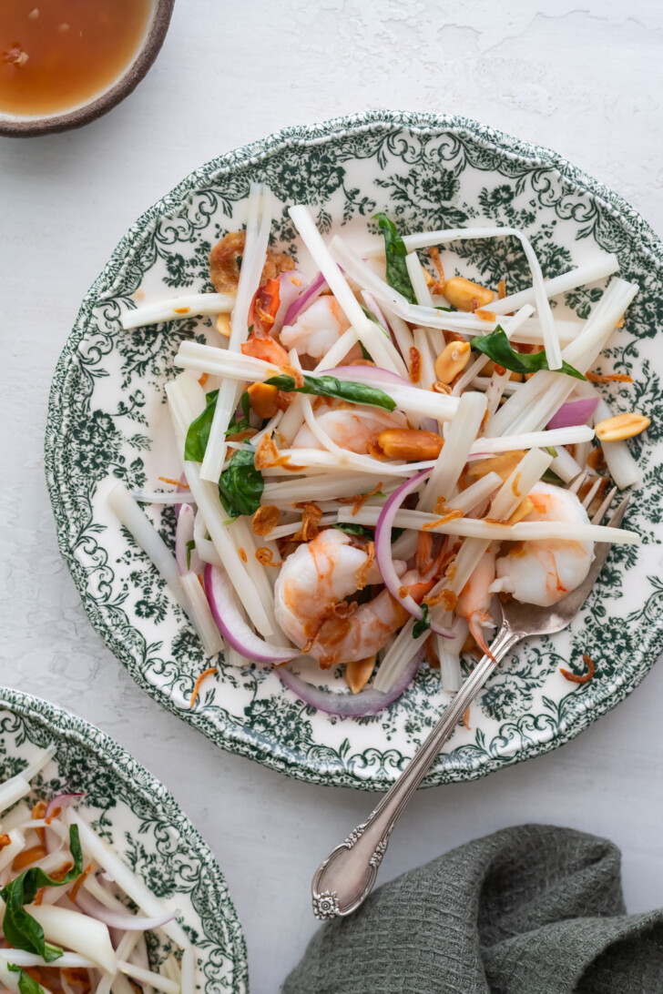Lotus stem salad served on a white plate with flowers. The salad is served with nuoc cham on the side.