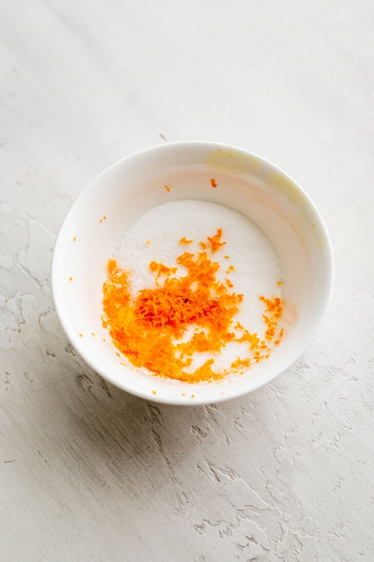 Orange zest and sugar in a white bowl.