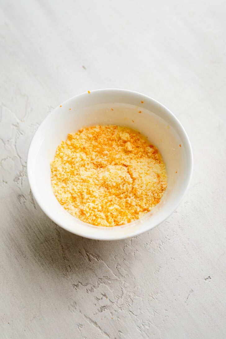 Sugar mixed together with orange zest in a white bowl.