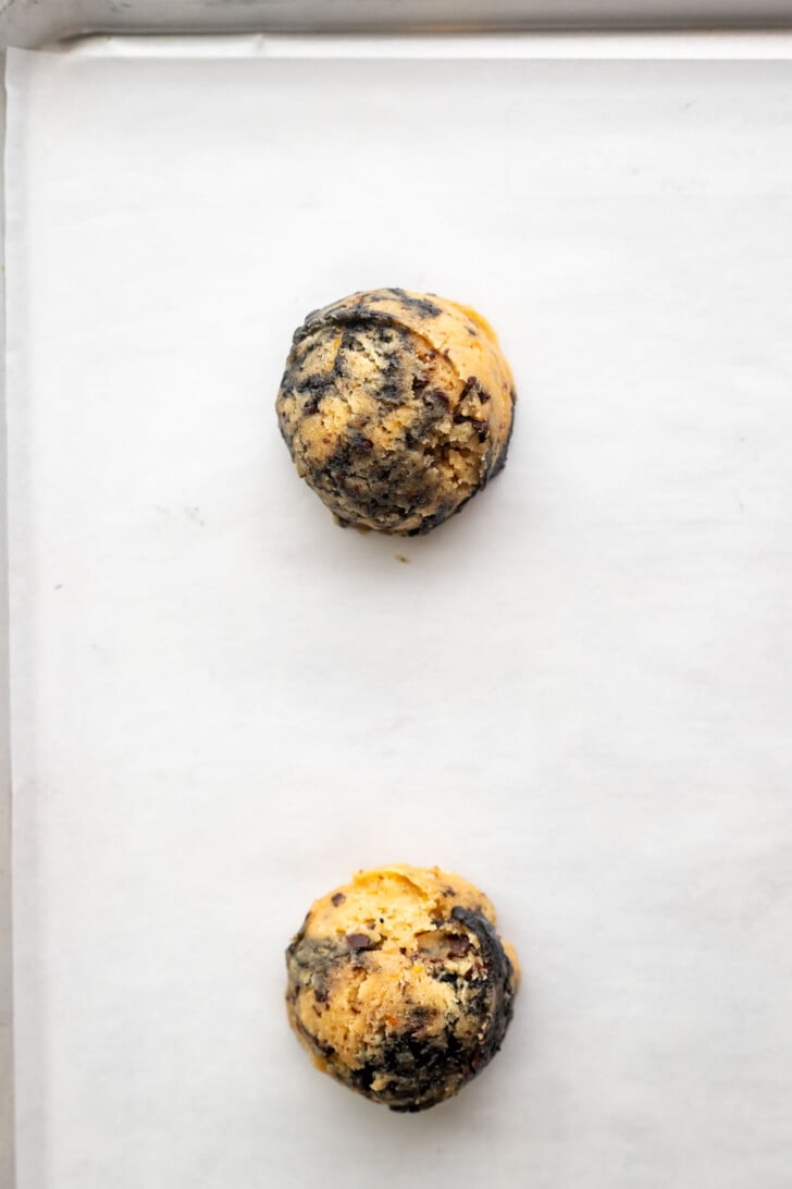Scooped orange black sesame cookie dough on a baking sheet.