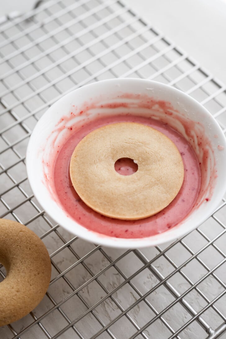 Dipping mochi donuts into a strawberry coconut glaze.