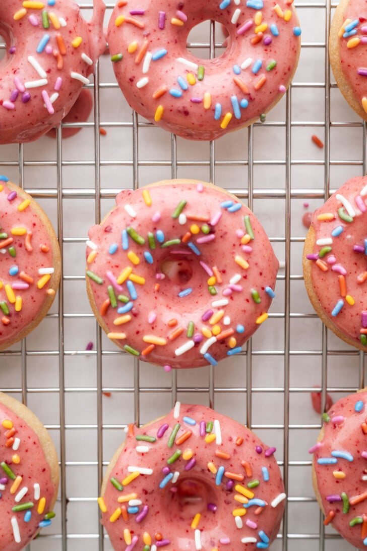 Strawberry mochi donuts drying on a cooling rack with sprinkles on top.