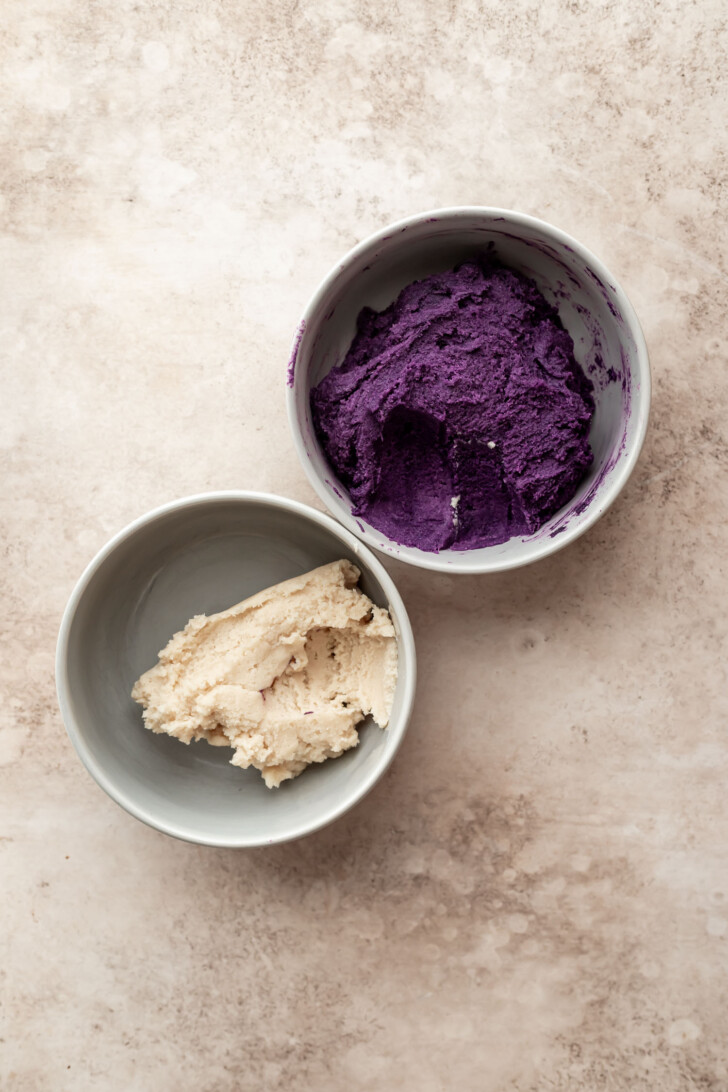 Two bowls on a light marble surface, one containing a smooth, bright purple mixture and the other holding a creamy, off-white mixture.