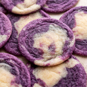Round cookies with a marbled pattern of purple and light beige dough, arranged overlapping on a light surface.