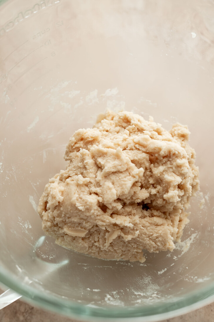 A ball of raw dough sits in a clear glass mixing bowl on a light countertop, ready to be shaped or baked.