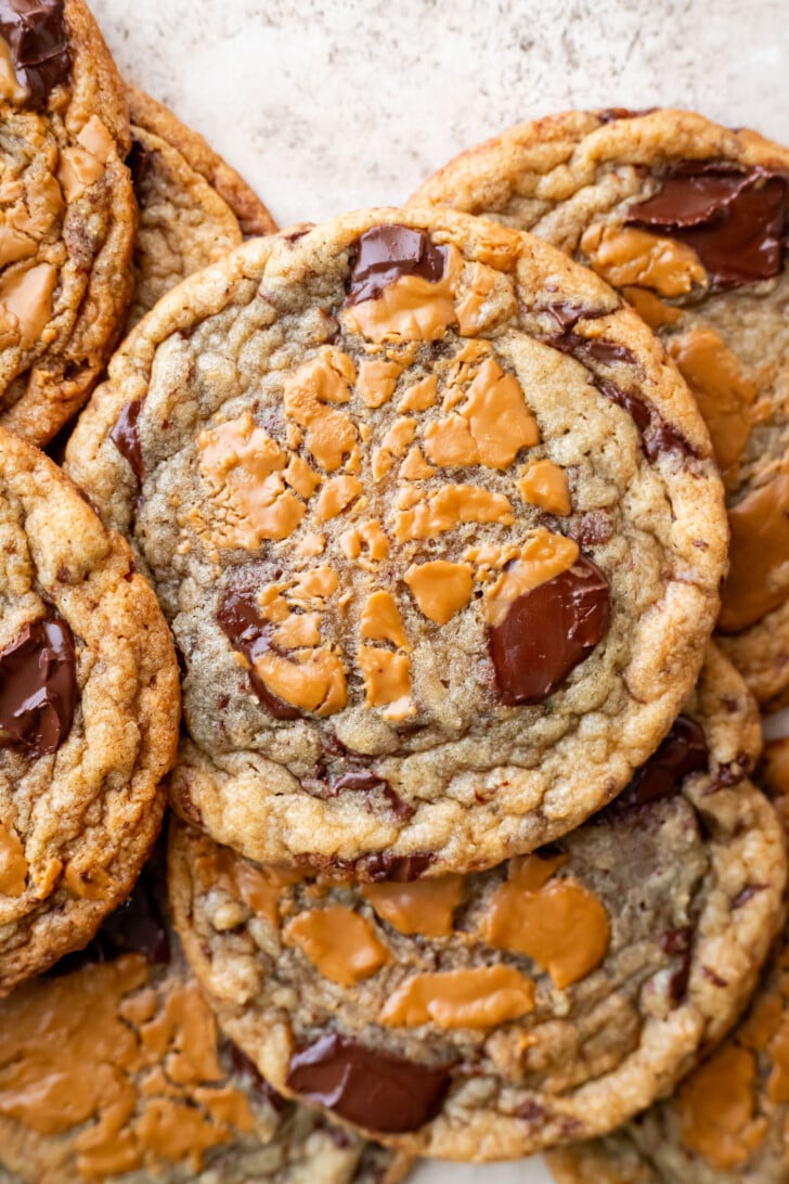 A close-up of several chocolate chip cookies with swirls of melted biscoff cookie butter on top, arranged in an overlapping pattern. The cookies have a golden-brown color and gooey chocolate chunks, reminiscent of decadent banana miso biscoff cookies.