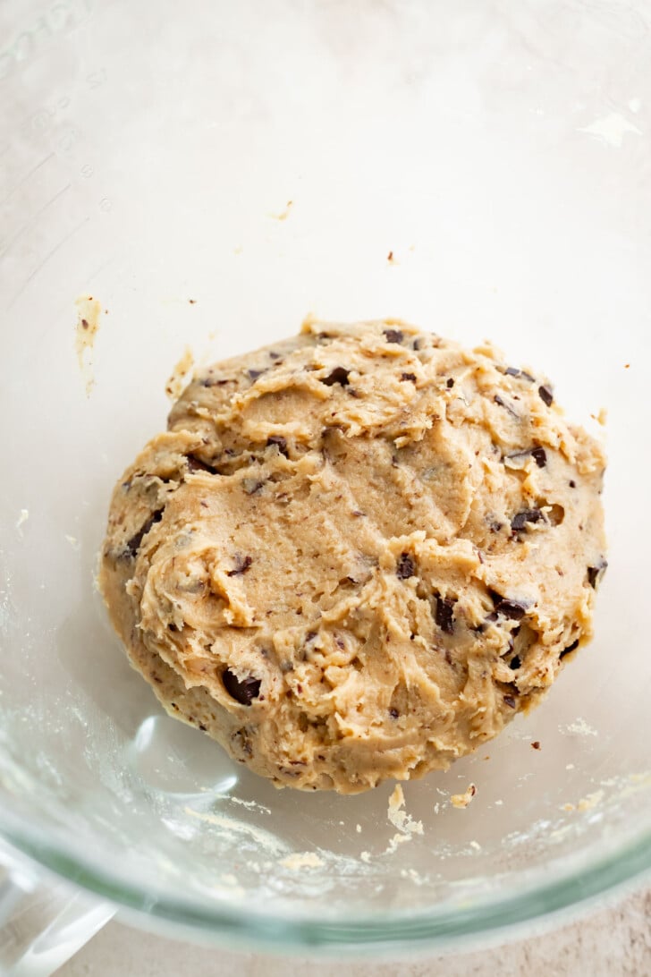 A glass mixing bowl containing a ball of banana miso chocolate chip cookie dough with visible chocolate chunks.