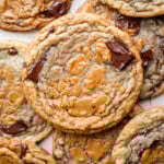 A close-up of several chocolate chip cookies with swirls of melted biscoff cookie butter on top, arranged in an overlapping pattern. The cookies have a golden-brown color and gooey chocolate chunks, reminiscent of decadent banana miso biscoff cookies.