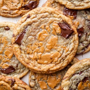 A close-up of several chocolate chip cookies with swirls of melted biscoff cookie butter on top, arranged in an overlapping pattern. The cookies have a golden-brown color and gooey chocolate chunks, reminiscent of decadent banana miso biscoff cookies.