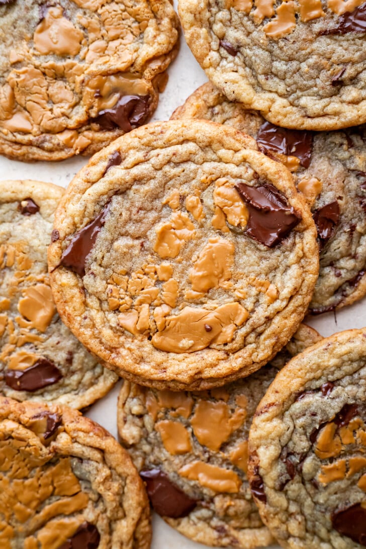 A close-up of several chocolate chip cookies with swirls of melted biscoff cookie butter on top, arranged in an overlapping pattern. The cookies have a golden-brown color and gooey chocolate chunks, reminiscent of decadent banana miso biscoff cookies.