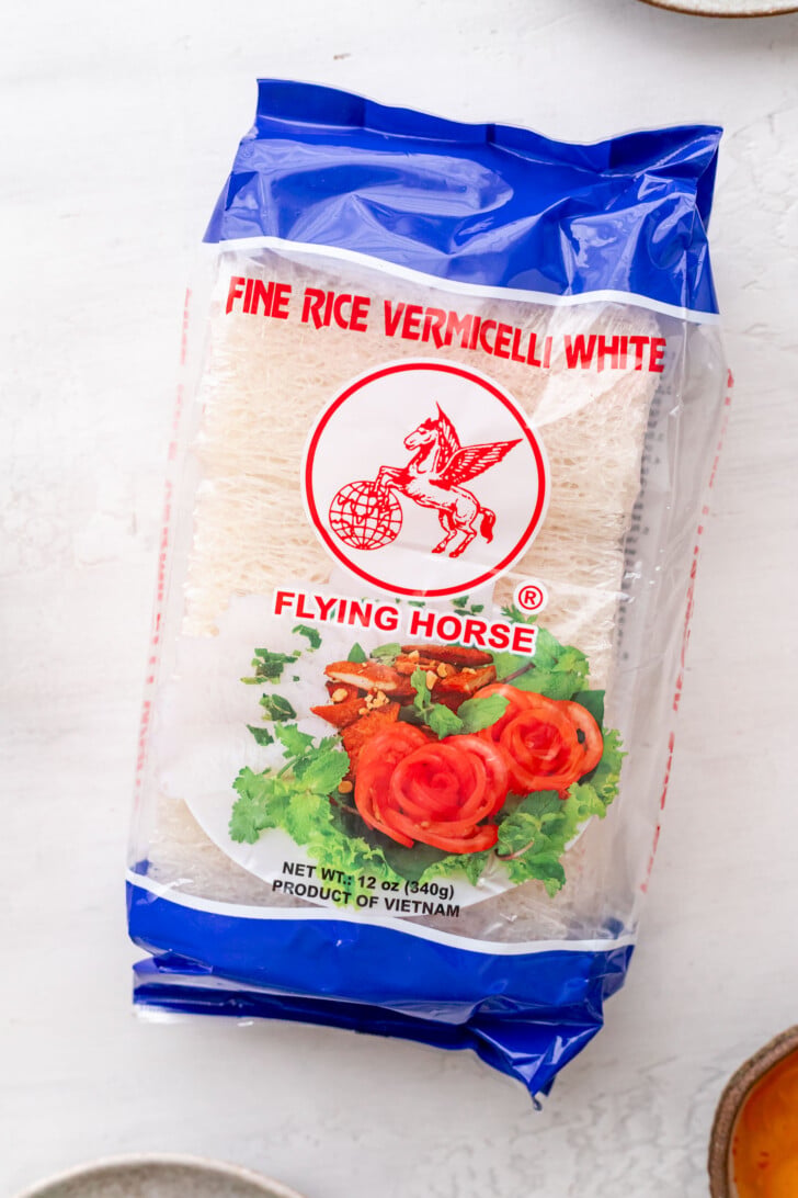 A package of Flying Horse fine rice vermicelli noodles, perfect for banh hoi, with a blue top, red text, and an image of tomatoes and lettuce, labeled as a 12 oz product of Vietnam.