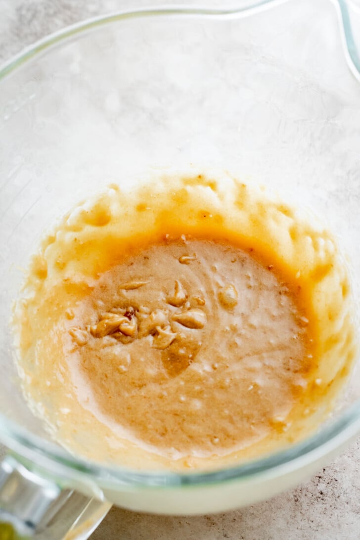 A clear mixing bowl containing a partially blended, light brown batter with visible small chunks, sitting on a light countertop.