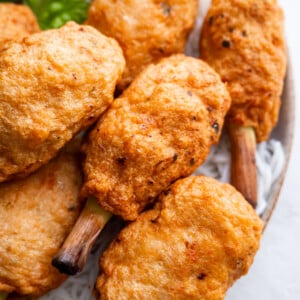 Golden brown chao tom skewers on lemongrass sticks are arranged on a plate with white vermicelli noodles and leafy greens visible in the background.
