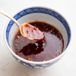 A ceramic bowl with a geometric blue pattern holds a dark, chunky sauce, with a spoon resting inside, coated in the sauce.