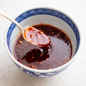 A ceramic bowl with a geometric blue pattern holds a dark, chunky sauce, with a spoon resting inside, coated in the sauce.