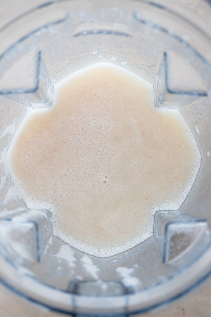 A close-up view of a blender containing a creamy, light beige lychee mixture, with some small bubbles visible on the surface.
