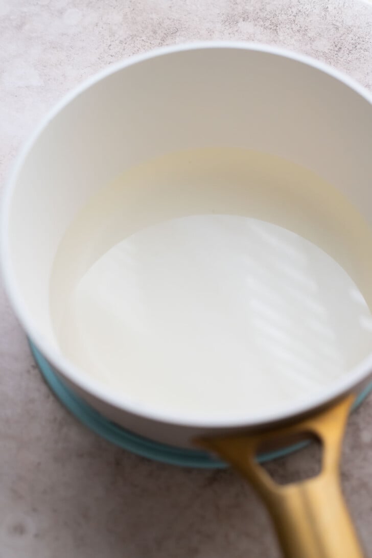 A white saucepan with a gold handle sits on a light countertop, filled with simple syrup