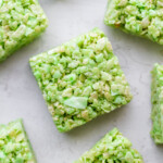 Close-up of green pandan rice krispie cereal treats cut into squares and arranged on a light surface.