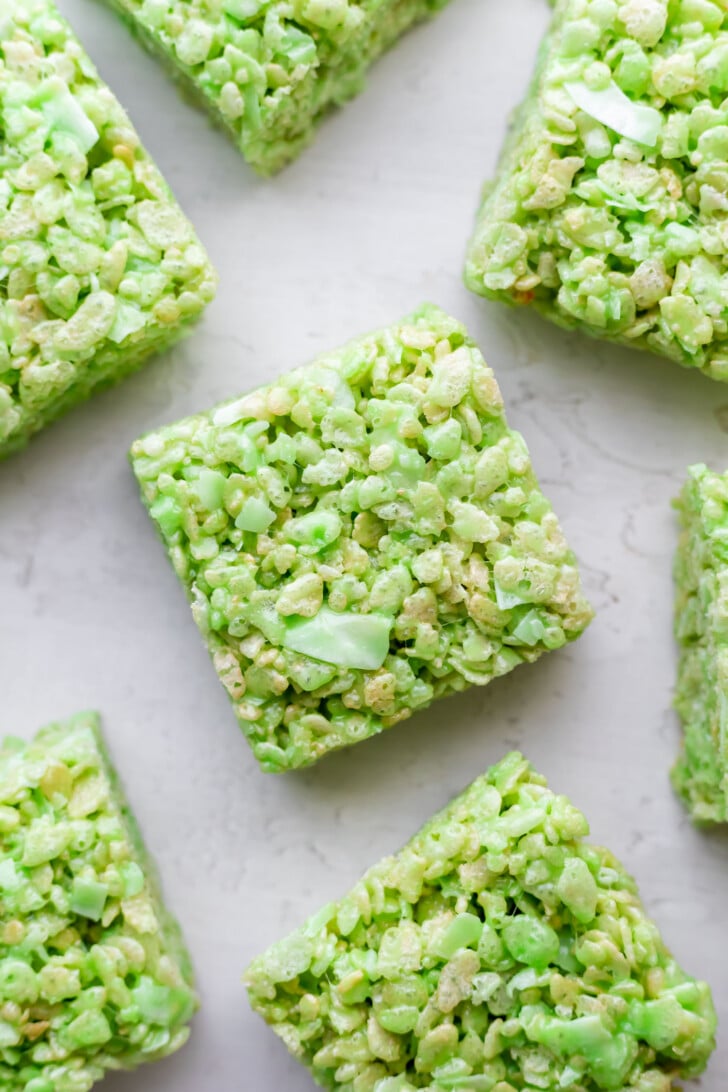 Close-up of green pandan rice krispie cereal treats cut into squares and arranged on a light surface.