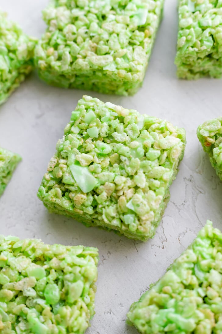 Several green pandan coconut Rice Krispie treats cut into squares are arranged on a light-colored surface. The treats have a crispy, textured appearance with visible cereal pieces.