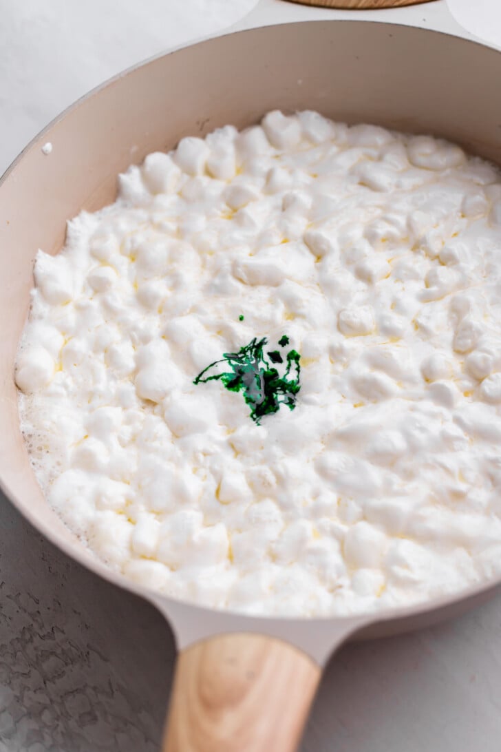 A pan filled with melted mini marshmallows topped with a small amount of pandan extract in the center.