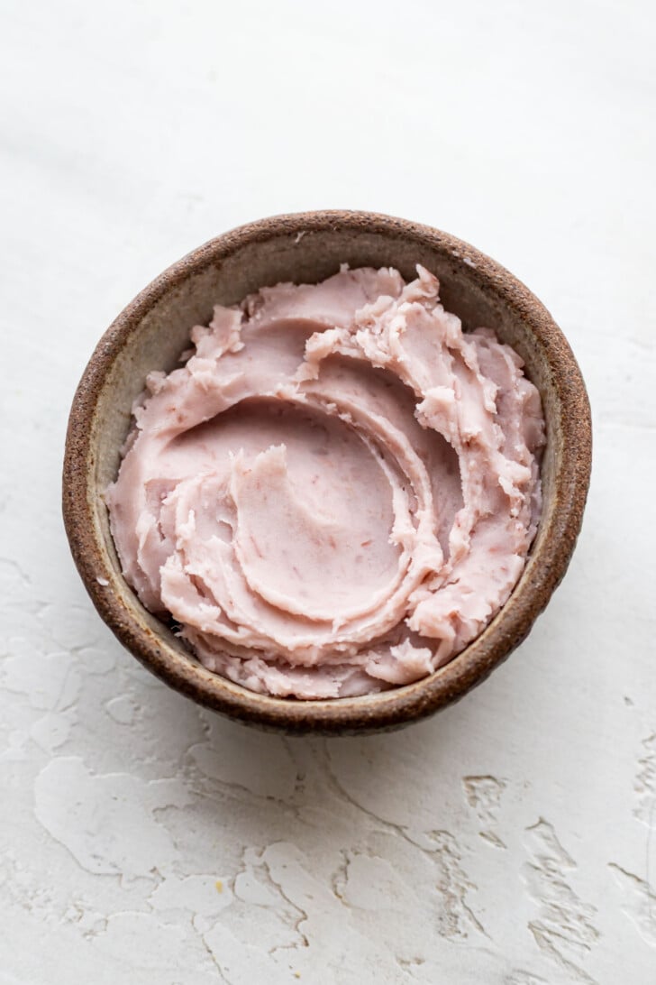 A small brown bowl filled with lavender taro paste placed on a textured white surface.