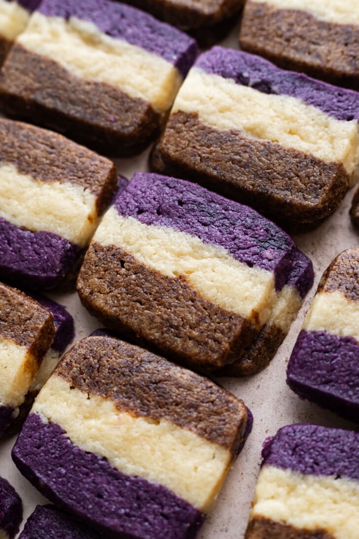 Rectangular cookies with three layers: a purple bottom and top, a brown middle, and a creamy white center. The cookies are arranged closely together on a flat surface.