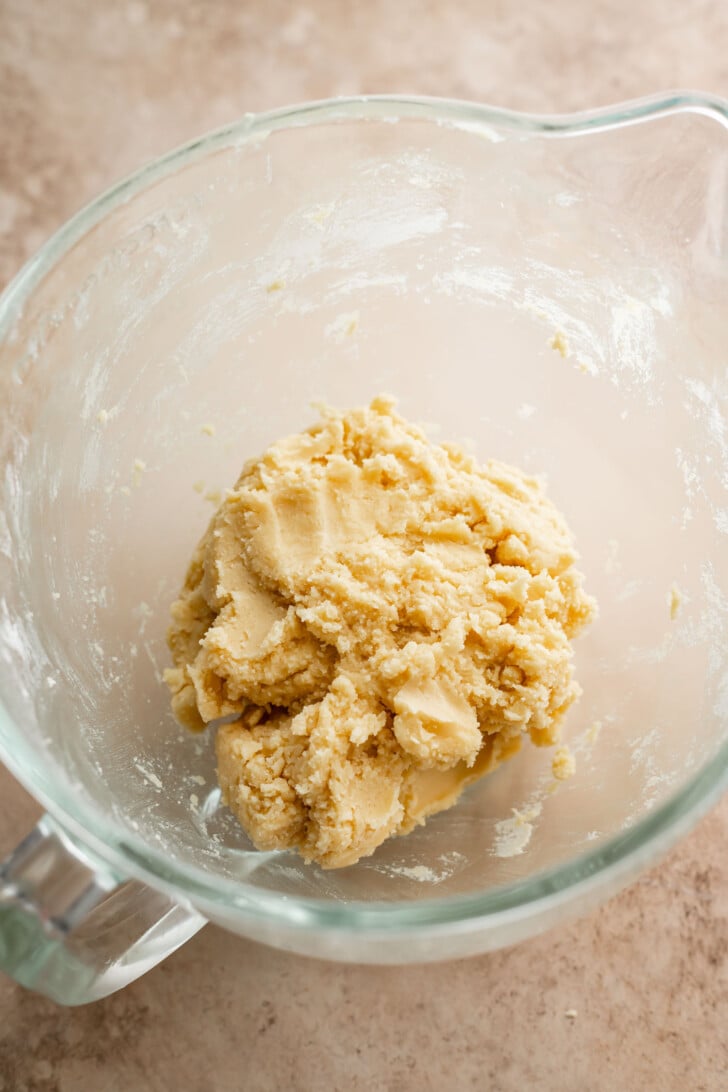 A glass mixing bowl with a ball of raw, pale yellow cookie dough pressed together, resting on a light-colored countertop.