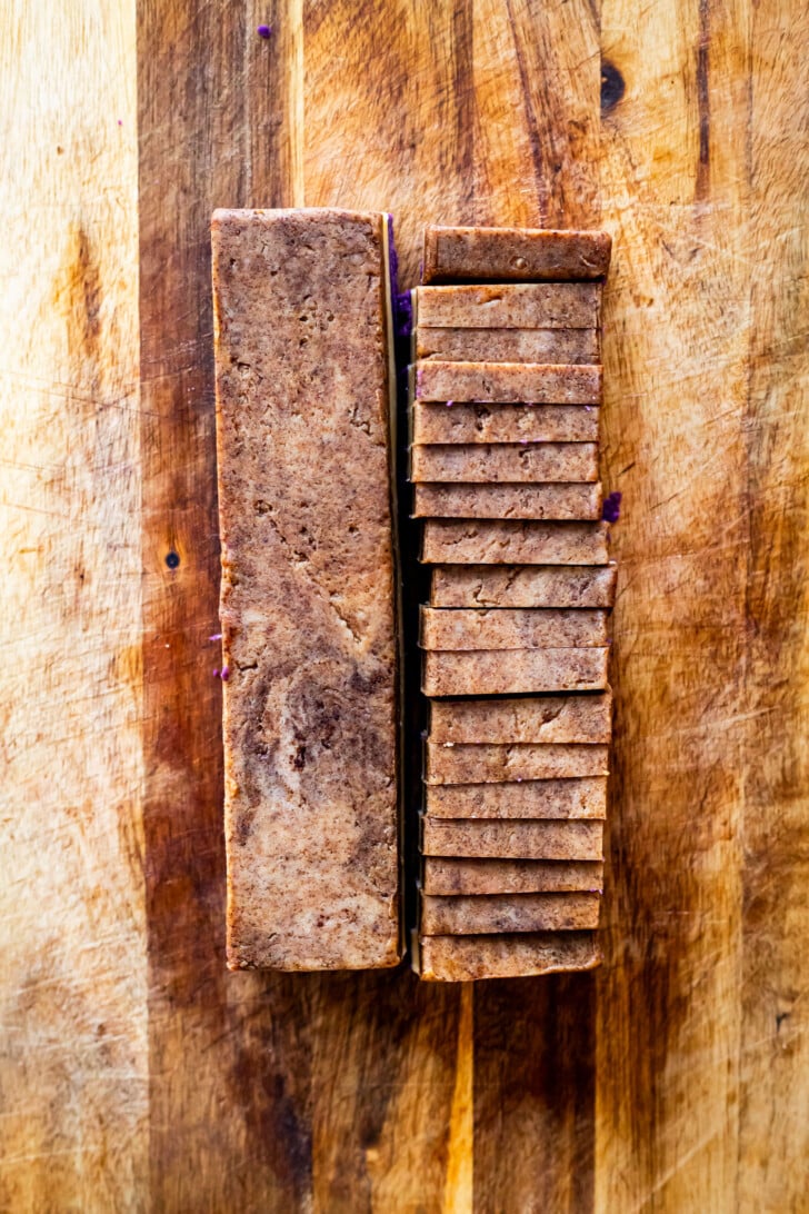 Rectangular loaf of bread on a wooden cutting board, with half of the loaf sliced into even pieces and the other half left whole.