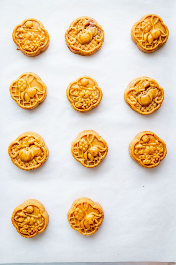 Twelve round mooncakes with intricate designs are evenly spaced on a sheet of white parchment paper.