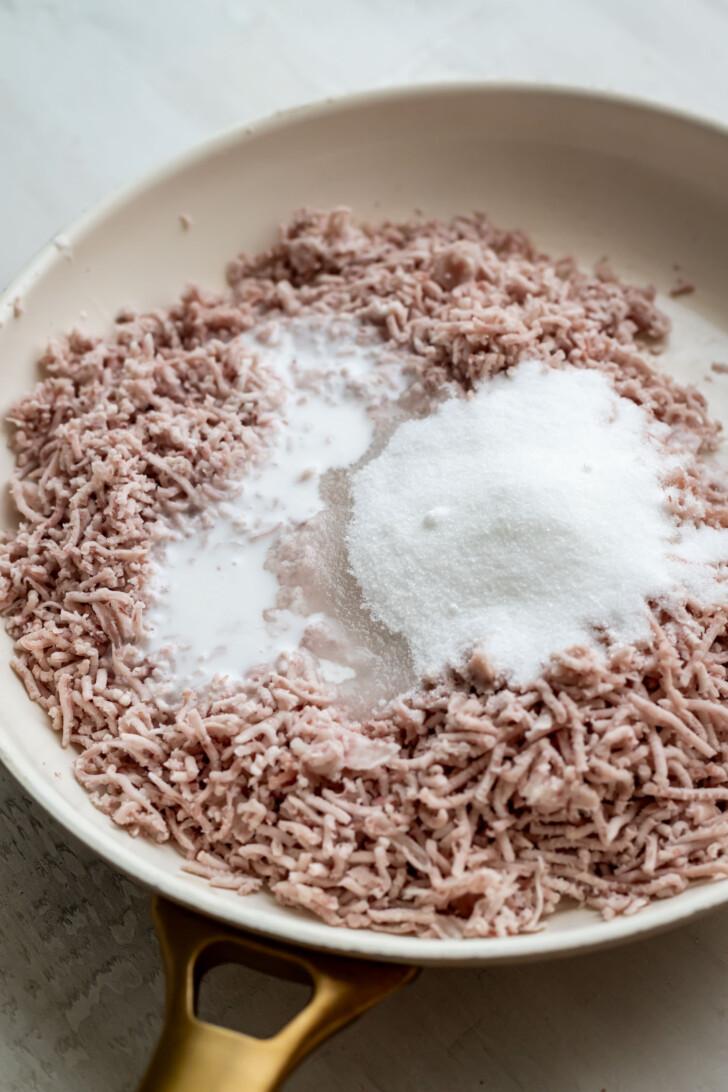 Mashed taro root in a pan with white sugar and coconut milk poured on top, ready to be mixed and cooked.