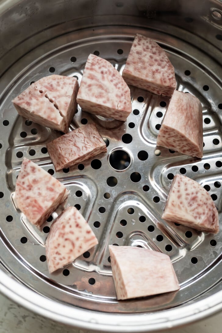 Steamer basket containing several chunks of steamed taro root with a speckled light purple and white appearance.