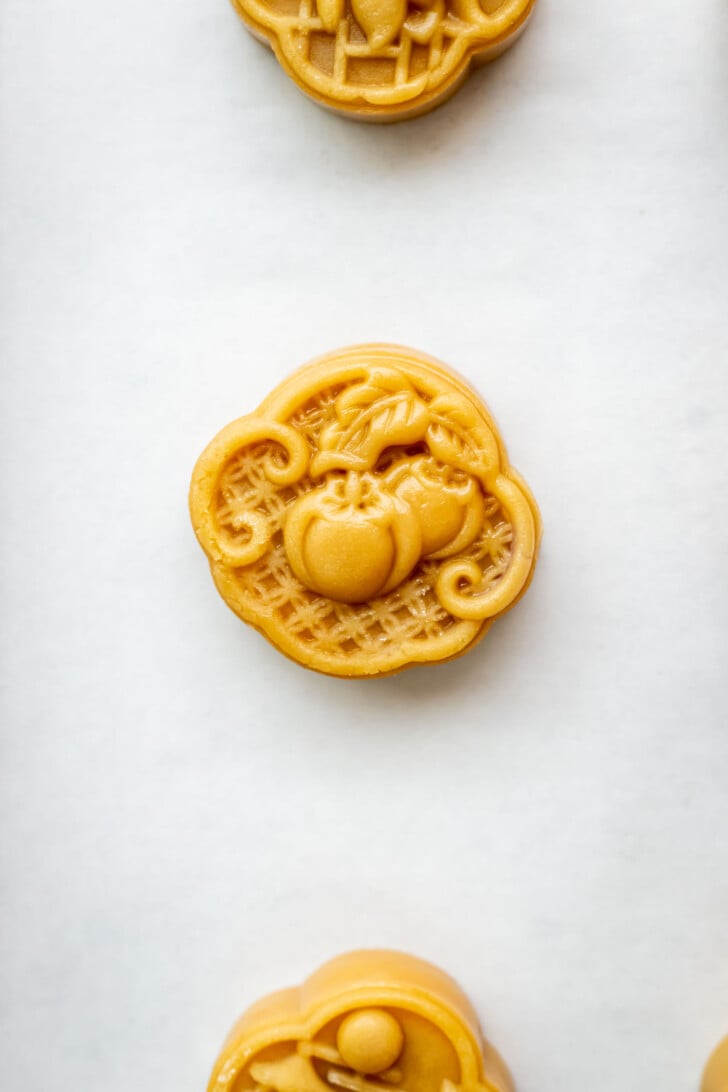 A round mooncake with an intricate design featuring a pumpkin and leaves on top, placed on a white background.