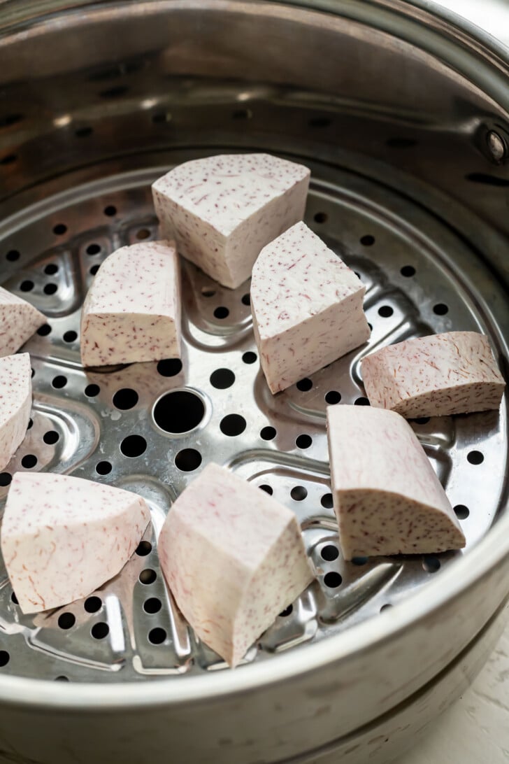 Chunks of raw taro root placed on a metal steamer tray, ready to be cooked.