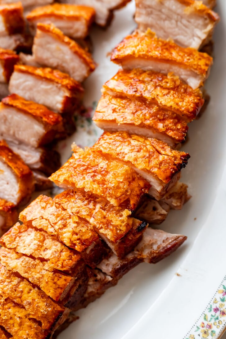 Close-up of sliced crispy pork belly with golden, crunchy skin and juicy meat, arranged neatly on a white platter.