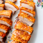 Sliced crispy pork belly with golden, crunchy skin arranged neatly on a floral-patterned plate.
