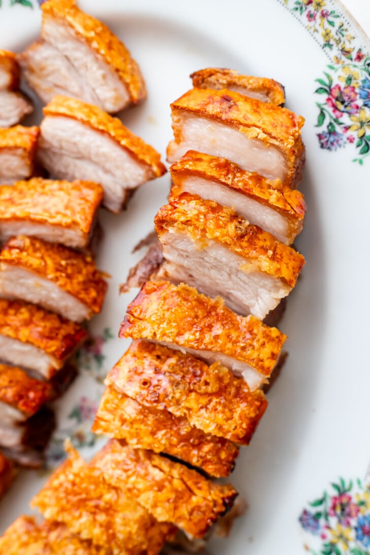 Sliced crispy pork belly with golden, crunchy skin arranged neatly on a floral-patterned plate.