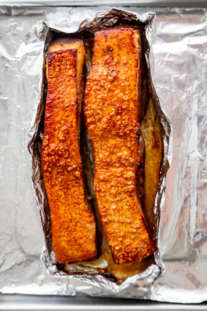 Two pieces of air fried pork belly with crispy, golden-brown skin sit on foil in a baking tray, showing a bubbly texture on the surface.